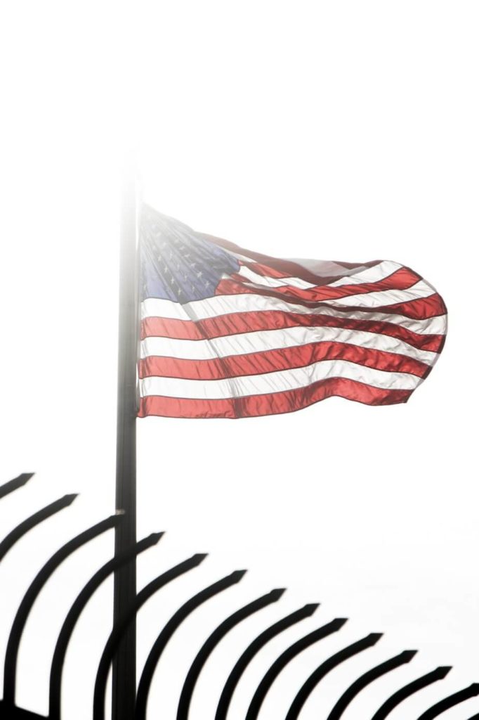 An American flag waving in the wind behind a black security fence.